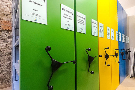 Büroarchiv mit grünen, gelben und blauen Vorsatzwänden sowie Drehsternantrieb und Regalbeschriftung